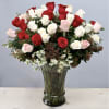 Tall vase of red, white, and pale pink roses with small white filler flowers.