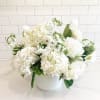 A lush, all-white arrangement featuring designer white hydrangeas, delicate white stock, and