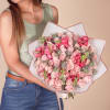 Woman holding a large bouquet of pink roses and snapdragons wrapped in white paper