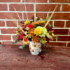 Mixed fall bouquet in a floral mug vase with daisies and mums