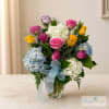 Mixed bouquet of roses and hydrangeas in a glass vase with a blue ribbon