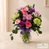 Mixed pink and purple bouquet in a glass vase with a purple ribbon