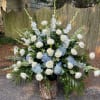 Large white and blue floral arrangement with roses and tall spikes in a wood base