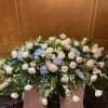 Large funeral spray of white roses and blue hydrangeas in a container