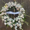 White rose wreath with orchids and a ribbon on a stand