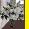 White lilies and roses arranged in a glass vase with blue flowers