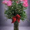 Pink roses in a clear glass vase with a red ribbon