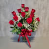 Red roses arranged in a clear glass vase with white baby's breath and a red ribbon.
