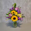Mixed bouquet of sunflowers, roses, and purple flowers in a glass vase