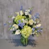 Blue and white flowers with pale green hydrangeas in a glass vase