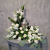 White roses and white flowers arranged around a silver urn on a table