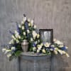 White calla lilies and roses arranged around a framed portrait and urn.