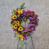 Heart-shaped floral wreath on a stand with sunflowers, roses, and purple blooms