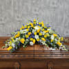 Large yellow, white, and blue floral spray on a wooden casket