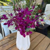 Purple orchids arranged in a white vase on a wooden table