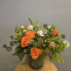 Bright orange roses take center stage in this garden-style flower arrangement, a