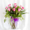 Pink roses in a glass vase with a purple ribbon