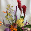 Tropical floral arrangement with red ginger, yellow orchids, and purple blooms in a black container