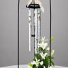 White lilies and roses arranged beneath a black wind chime stand