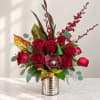 Red roses arranged in a silver vase with burgundy orchids and patterned leaves