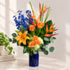 Orange roses, lilies, and blue delphinium in a cobalt vase