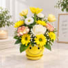 Yellow and white flower arrangement in a smiley-face pot