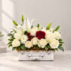 White lilies and roses arranged in a white suitcase-style container