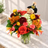 Autumn bouquet of mixed flowers in a clear glass vase with a scarecrow topper