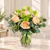 Peach roses and green orchids in a glass vase with a ribbon