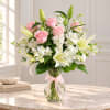 Pink roses and white lilies in a clear glass vase with a pink ribbon