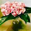 Pink rose bouquet in a clear glass vase with large green leaves