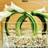 White calla lilies arranged in a clear rectangular vase with white stones