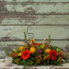 Low floral centerpiece with red gerbera daisies and yellow roses in a glass container