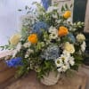 Mixed bouquet of blue hydrangeas, white daisies, and yellow roses in a basket