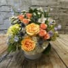 Mixed bouquet of peach roses, hydrangeas, and blue thistle in a white vase