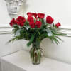 Red roses arranged in a clear glass vase with greenery