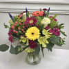Bright mixed bouquet of gerbera daisies, roses, and other blooms in a clear glass vase