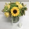 Yellow roses and a sunflower in a glass vase with a small candle nearby
