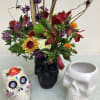 Floral arrangement in a black skull vase with colorful skull planters beside it