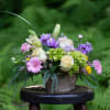 Mixed bouquet in a rustic container with pink, purple, white, and green blooms