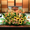 Large stage arrangement of yellow sunflowers and orange blooms in a low spray in front of a podium