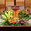 Large tropical stage arrangement with yellow spikes, orange lilies, and birds of paradise before a podium