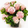 Pink roses arranged in a clear square vase with green berries