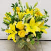 Yellow lilies and roses arranged in a clear glass vase