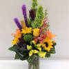 Colorful bouquet with sunflowers, lilies, and purple spikes in a glass vase