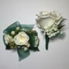 Two white rose boutonnieres with green ribbon and baby's breath