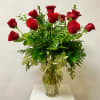 Red roses arranged in a clear glass vase with mixed greenery