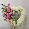Heart-shaped white floral wreath with pink roses and carnations on a stand