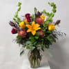Mixed bouquet with orange lily, red and yellow roses in a glass vase