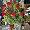 Tall vase arrangement of red roses with mixed greenery and a red ribbon